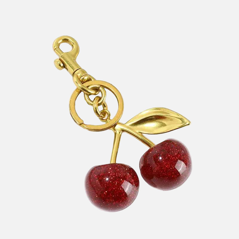 Gold keychain with red cherry-like charms on a white background