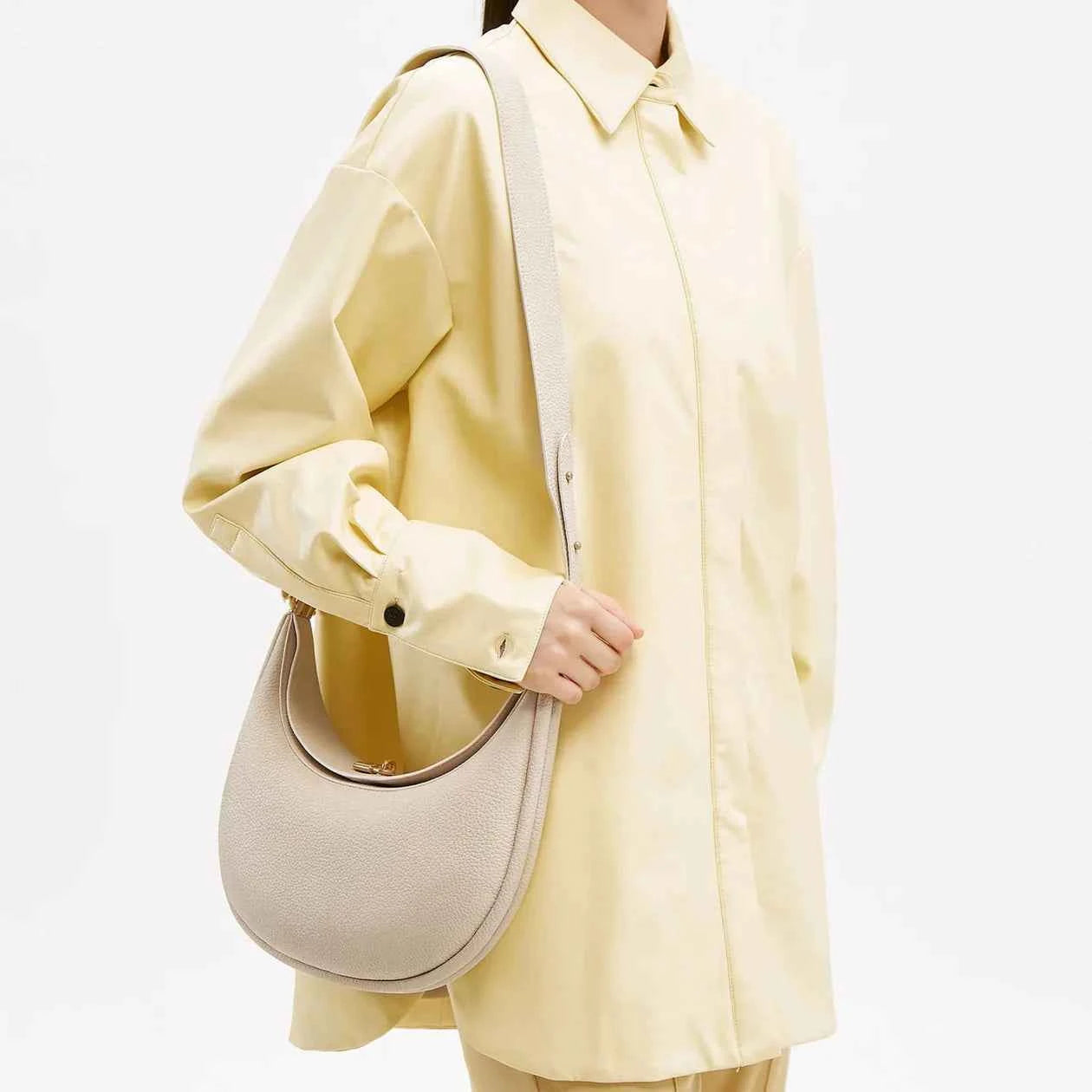 Person wearing a light yellow coat holding a beige luna bag on a white background