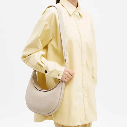 Person wearing a light yellow coat holding a beige luna bag on a white background