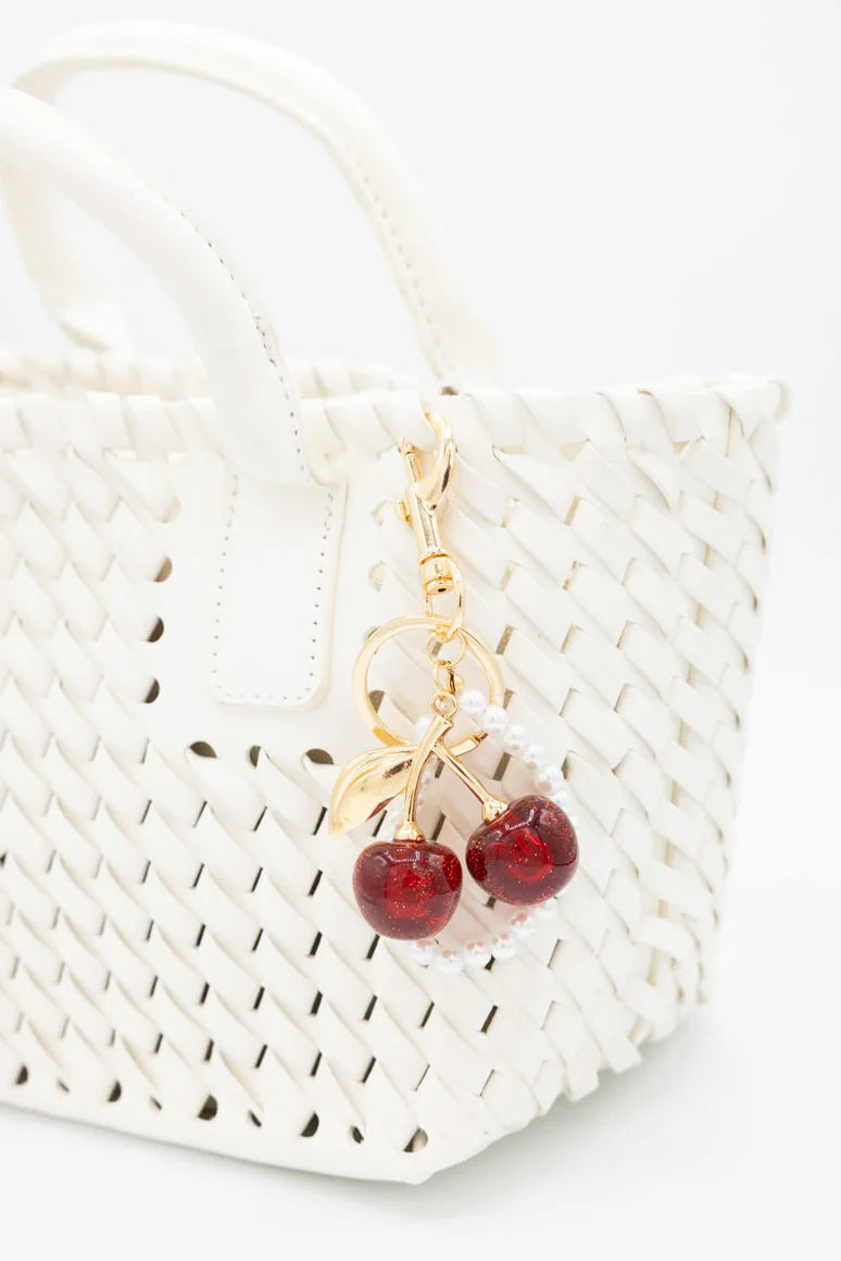 Gold and red cherry-shaped keychain on a white woven bag