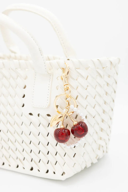 Gold and red cherry-shaped keychain on a white woven bag